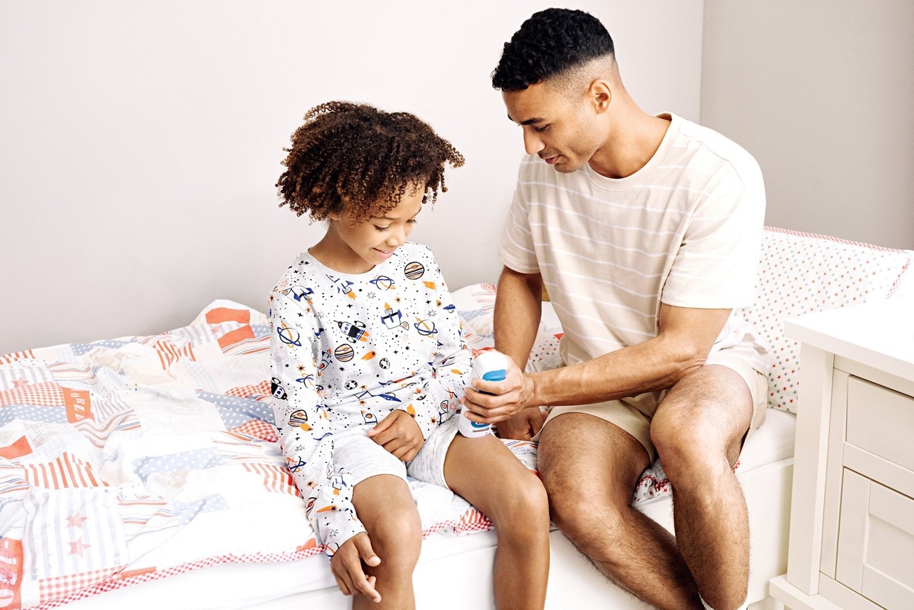 Female child sitting on adult male's lap on a couch. Adult female also sitting on couch holding papers and speaking to the child and man.